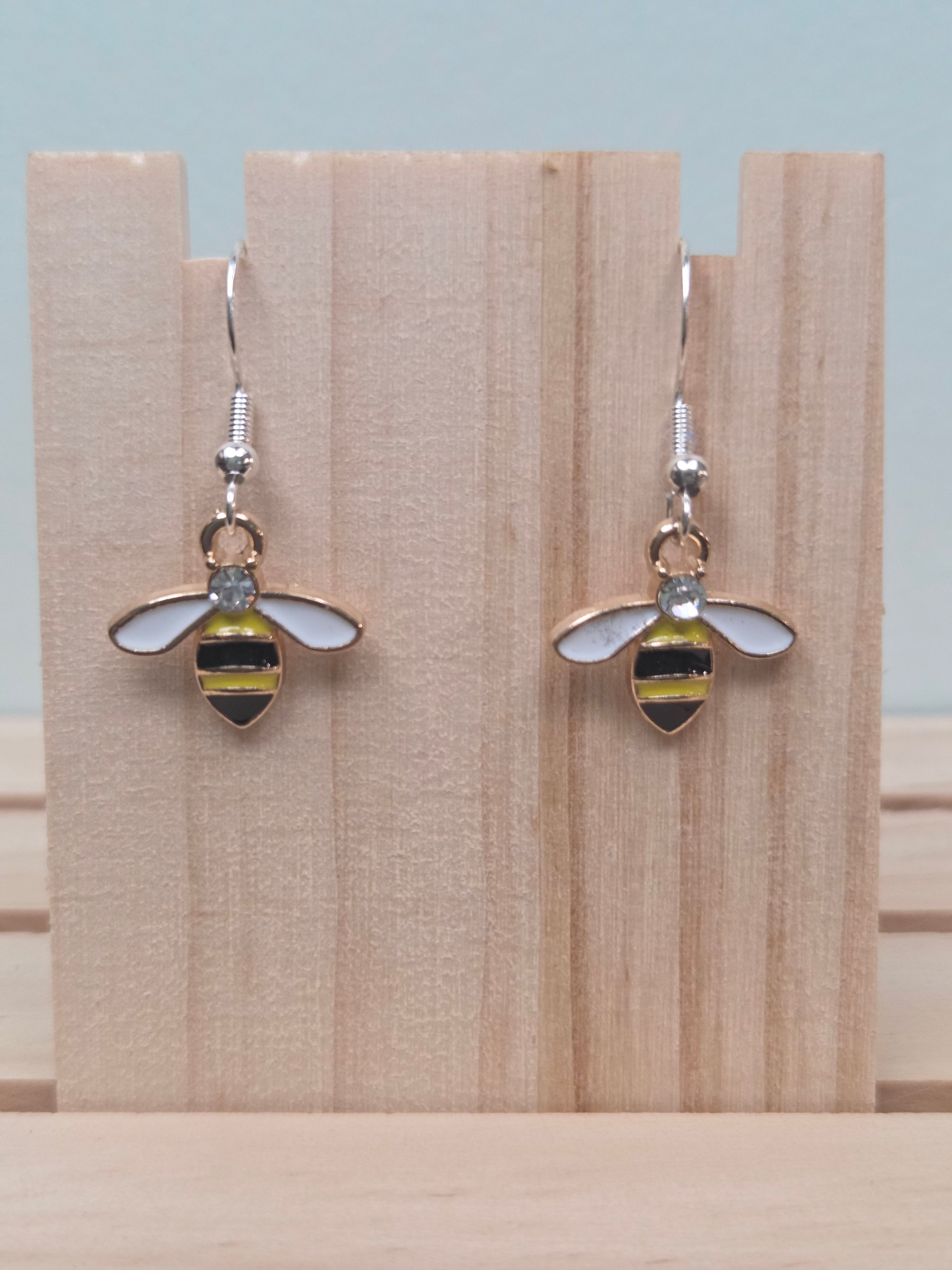 Gold-tone enamel bee dangle earrings with black, yellow, and white body and crystal accent, shown on wood display