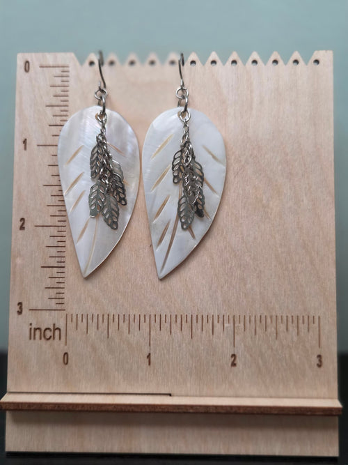 Mother of pearl leaf earrings with silver charm drops shown on a ruler display stand, approximately 2.5 inches in length