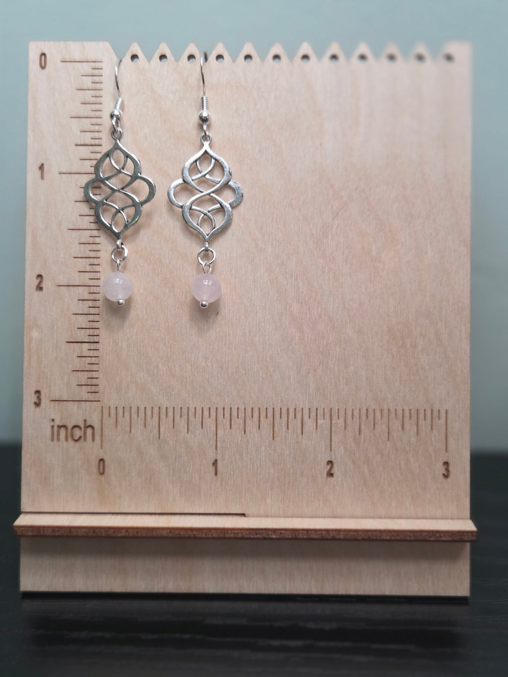 Rose quartz swirl knot dangle earrings against ruler showing approximately 2 inch length
