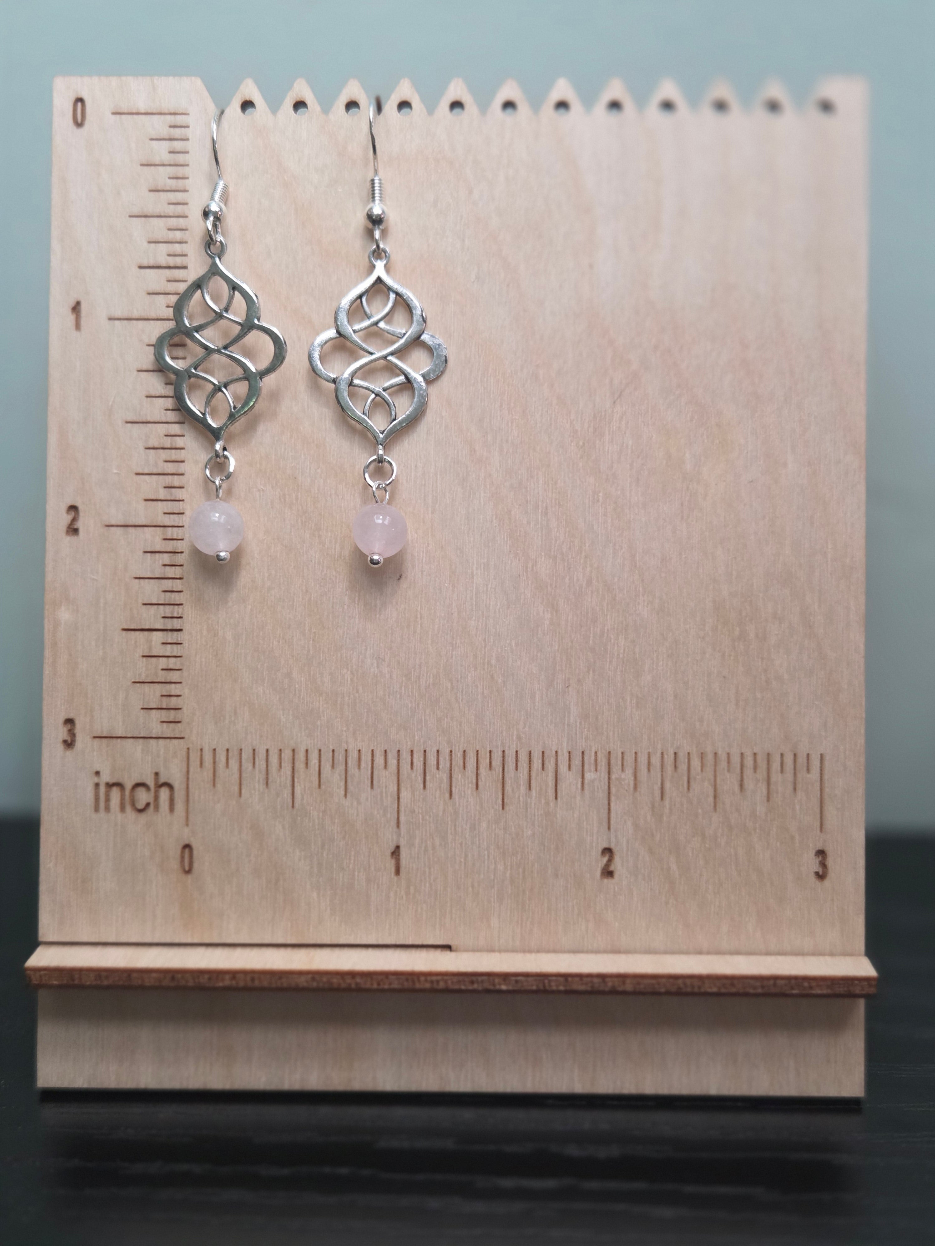 Rose quartz swirl knot dangle earrings against ruler showing approximately 2 inch length