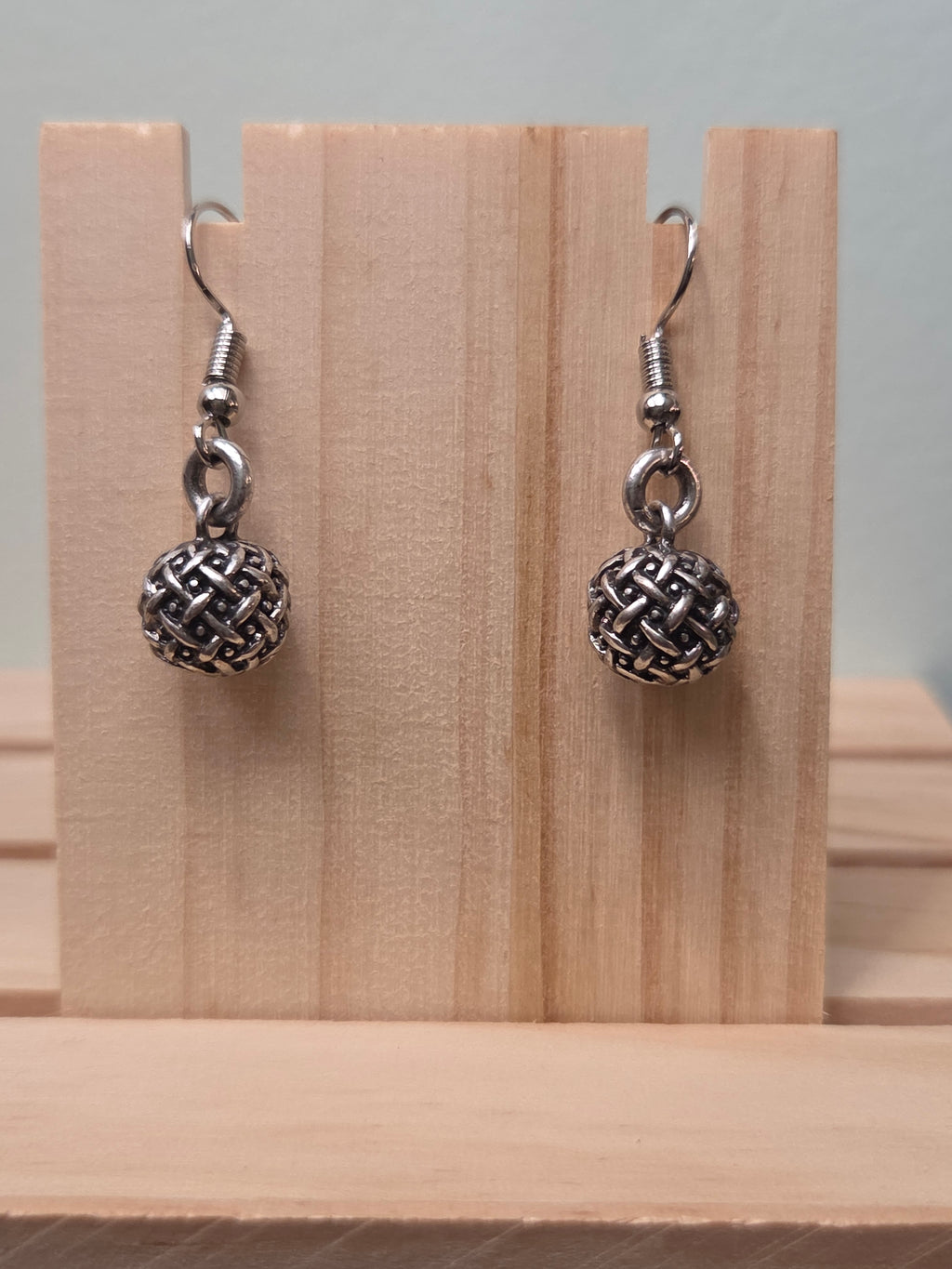 Pair of small silver-tone woven texture ball drop earrings, shown on a wooden ruler stand measuring approximately 1 inch