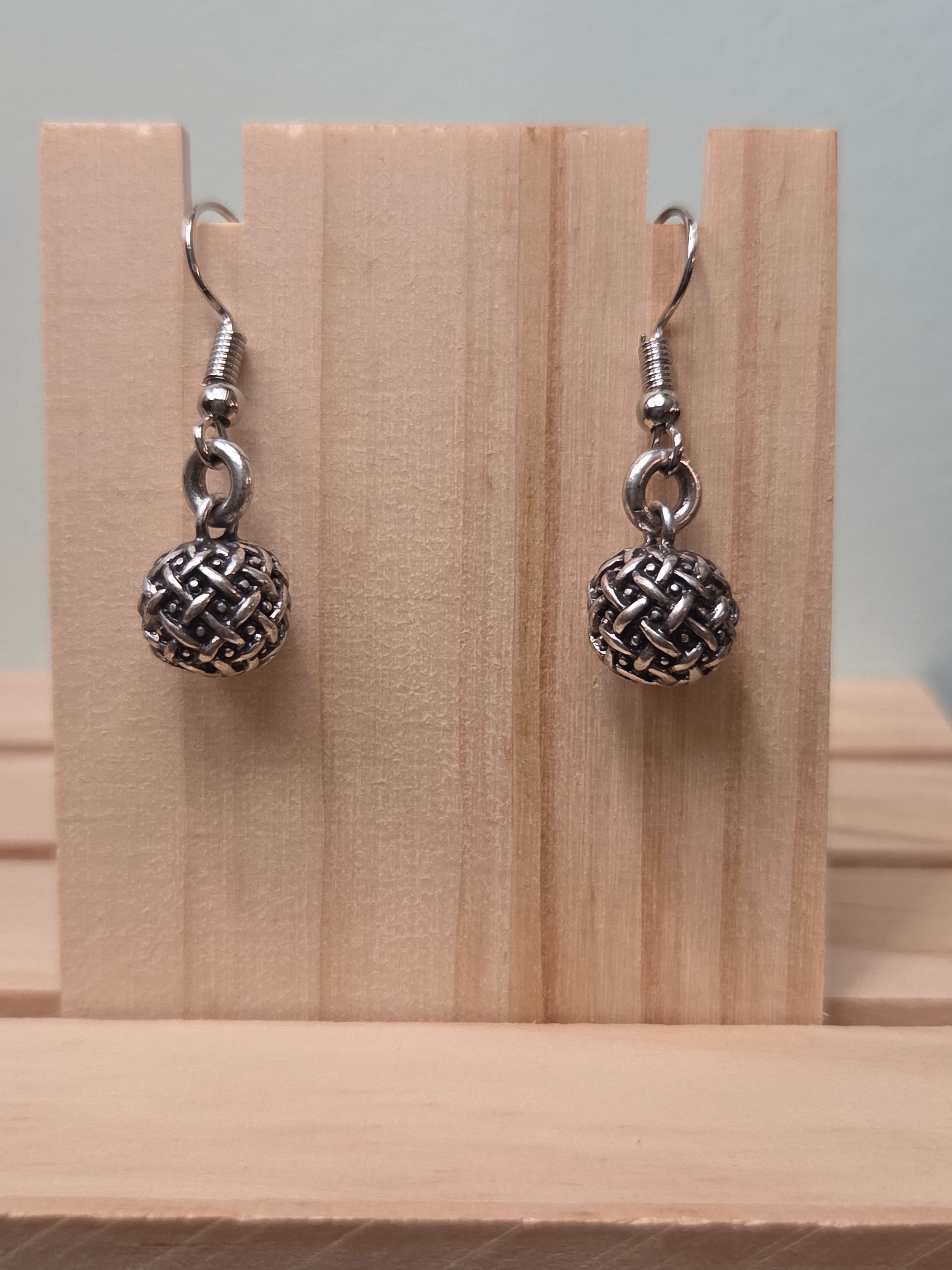 Pair of small silver-tone woven texture ball drop earrings, shown on a wooden ruler stand measuring approximately 1 inch