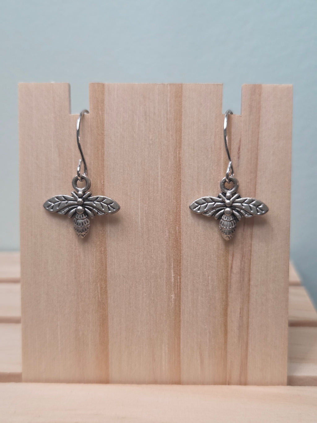 Silver-tone bee charm dangle earrings, shown on wood display