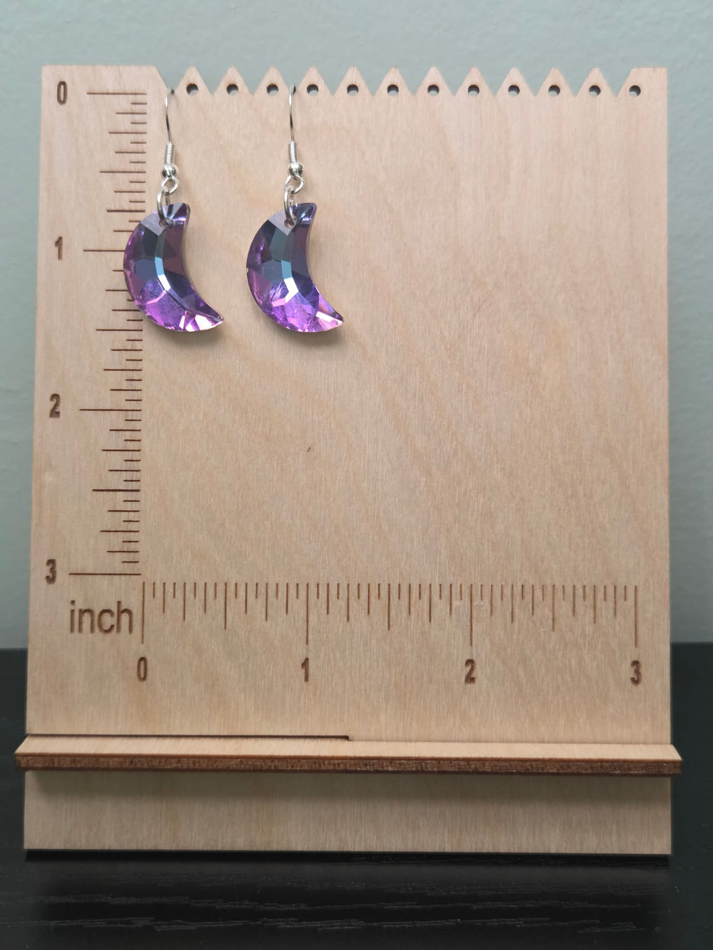 Faceted purple crystal crescent moon drop earrings on wooden display stand with ruler showing approximately 1.75 inches in length