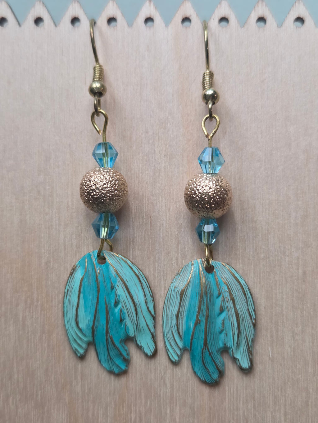 Turquoise and gold painted patina leaf drop earrings with blue crystal bicone and textured gold bead, flat lay on white background