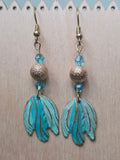 Turquoise and gold painted patina leaf drop earrings with blue crystal bicone and textured gold bead, flat lay on white background