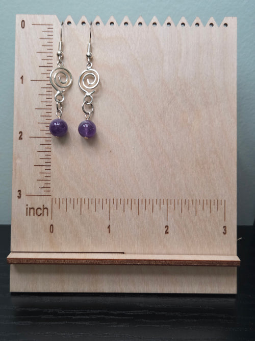 Close-up of amethyst spiral earrings showing silver-tone spiral charm and deep violet amethyst bead on wood grain surface