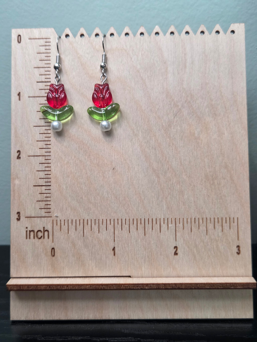 Close-up of glass tulip flower earrings with green leaf bead and white glass pearl accent on wood grain surface
