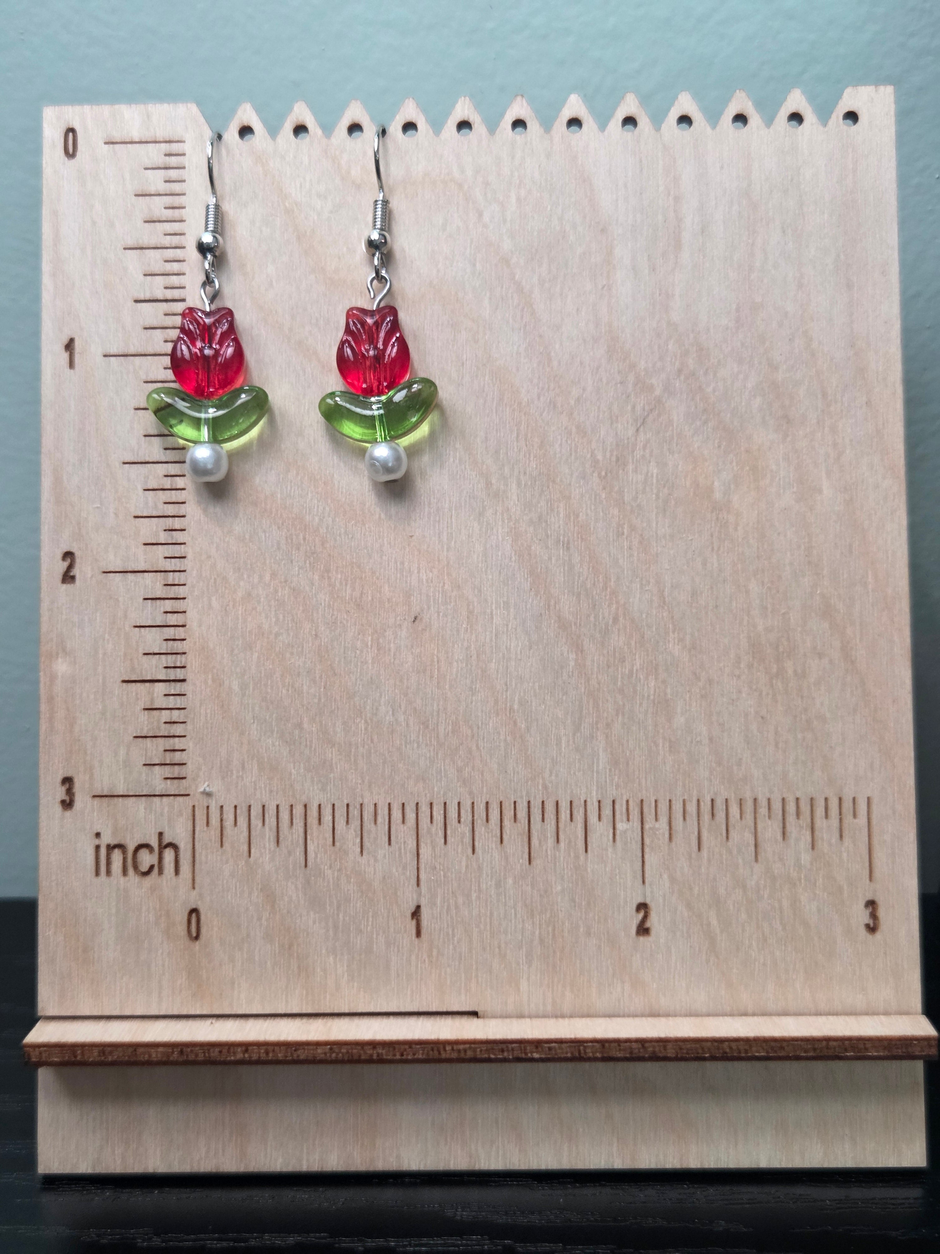 Close-up of glass tulip flower earrings with green leaf bead and white glass pearl accent on wood grain surface