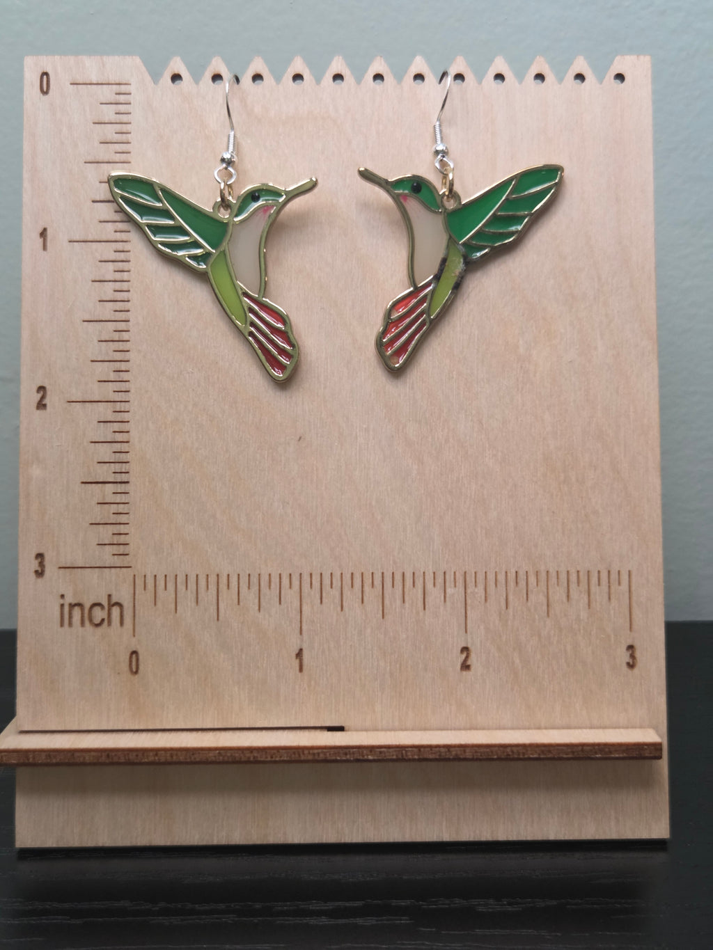 Stained glass style acrylic hummingbird dangle earrings against ruler showing approximately 1.4 inch length