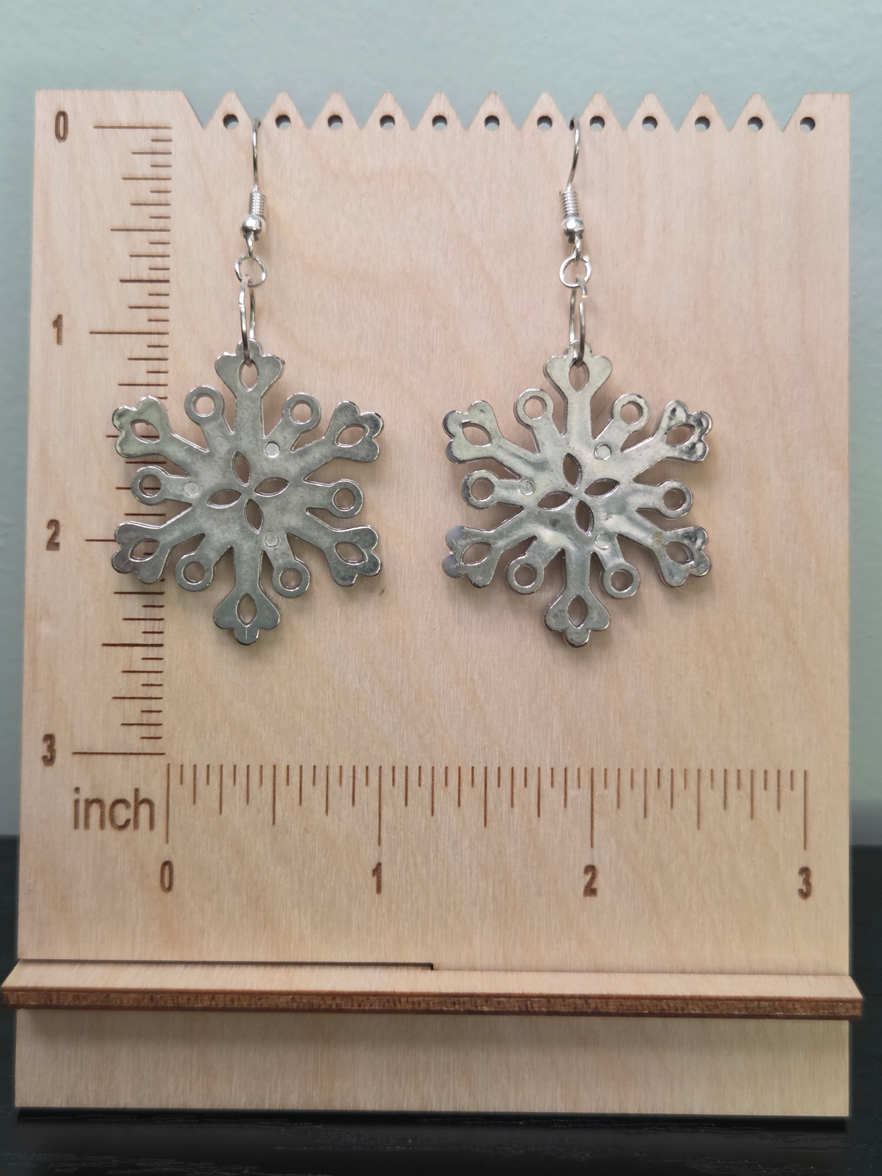 Small acrylic snowflake drop earrings displayed on a wooden earring stand with ruler showing approximately 1.75 inch length