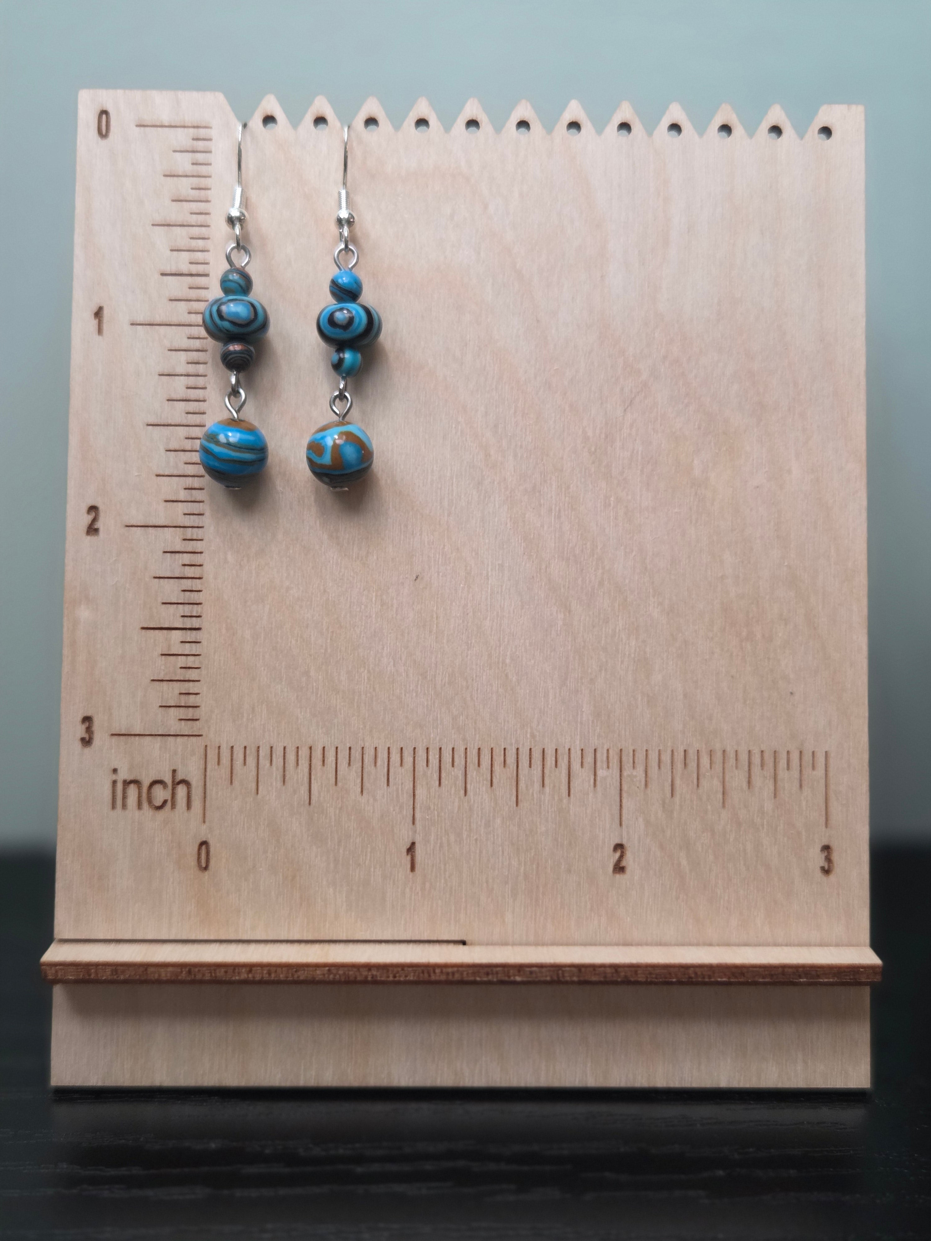 Mystery stone graduated drop earrings shown on a wooden ruler stand measuring approximately 1.75 inches, in turquoise, black, and tan swirl