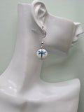 White round glass bead earring with blue painted dragonfly motif, shown on white mannequin ear with silver-tone hook, natural lighting