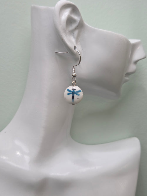 White round glass bead earring with blue painted dragonfly motif, shown on white mannequin ear with silver-tone hook, natural lighting