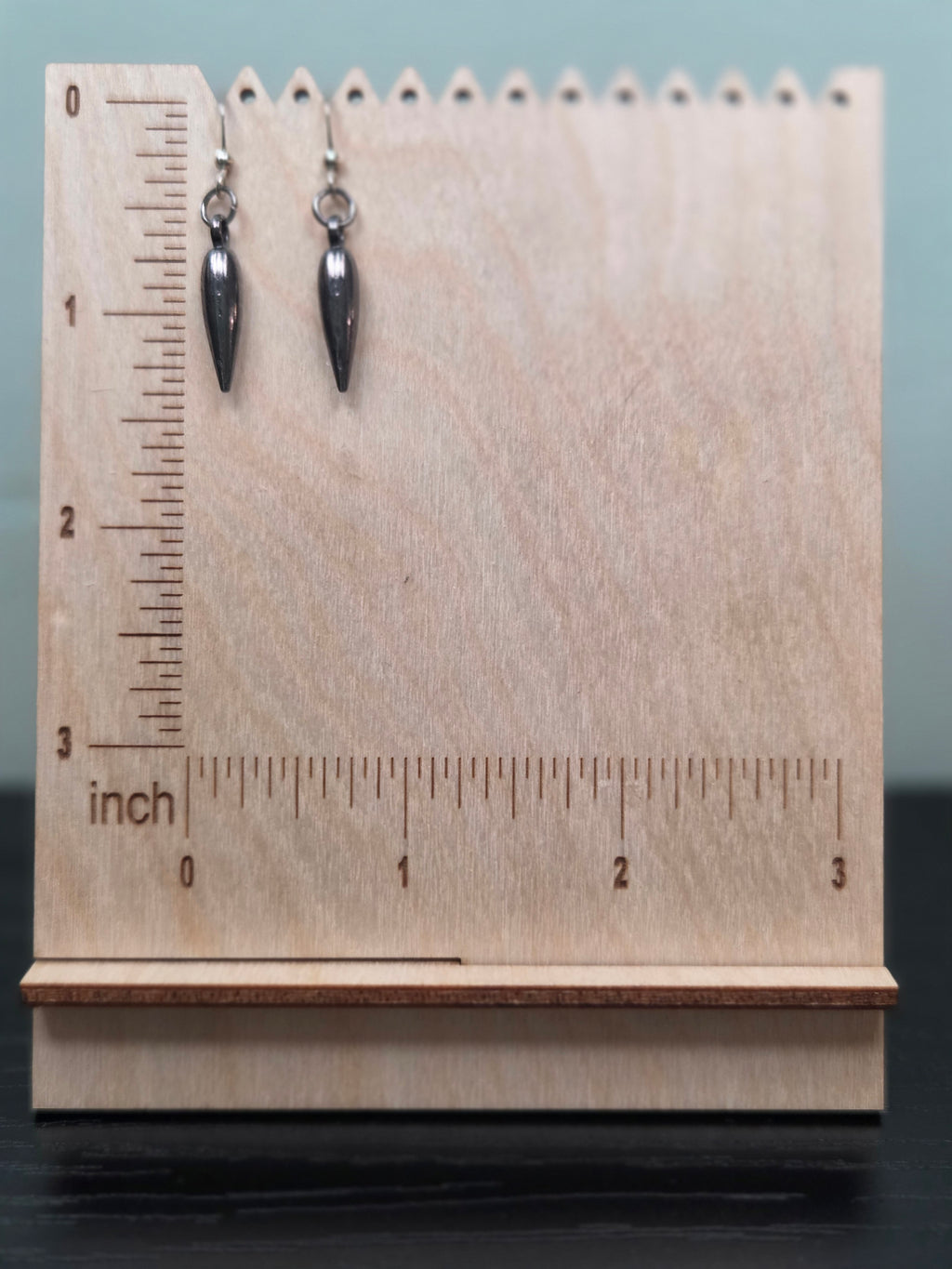 Gunmetal teardrop spike charm dangle earrings against ruler showing approximately 1 inch length