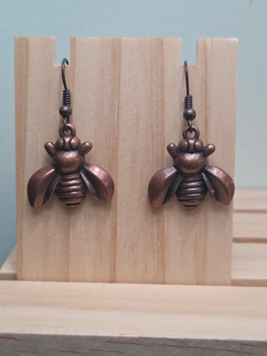 Antiqued copper-tone bee charm dangle earrings, shown on wood display
