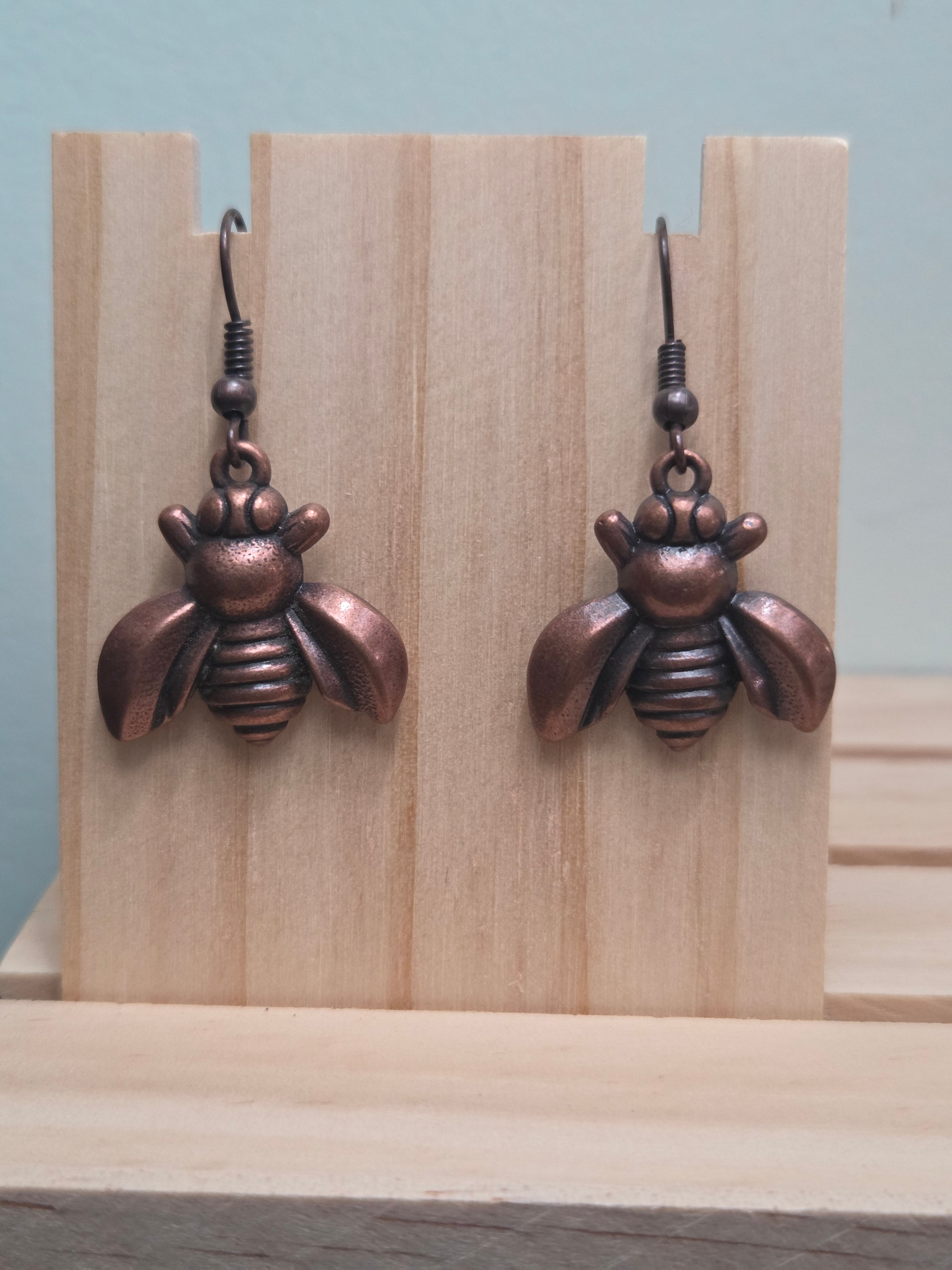 Antiqued copper-tone bee charm dangle earrings, shown on wood display
