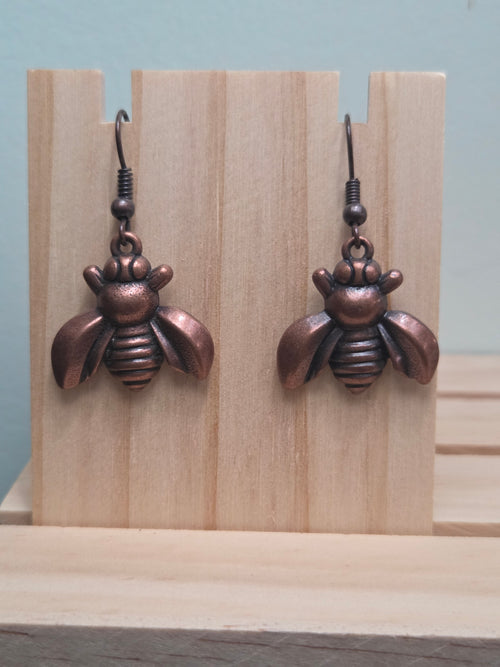 Antiqued copper-tone bee charm dangle earrings, shown on wood display
