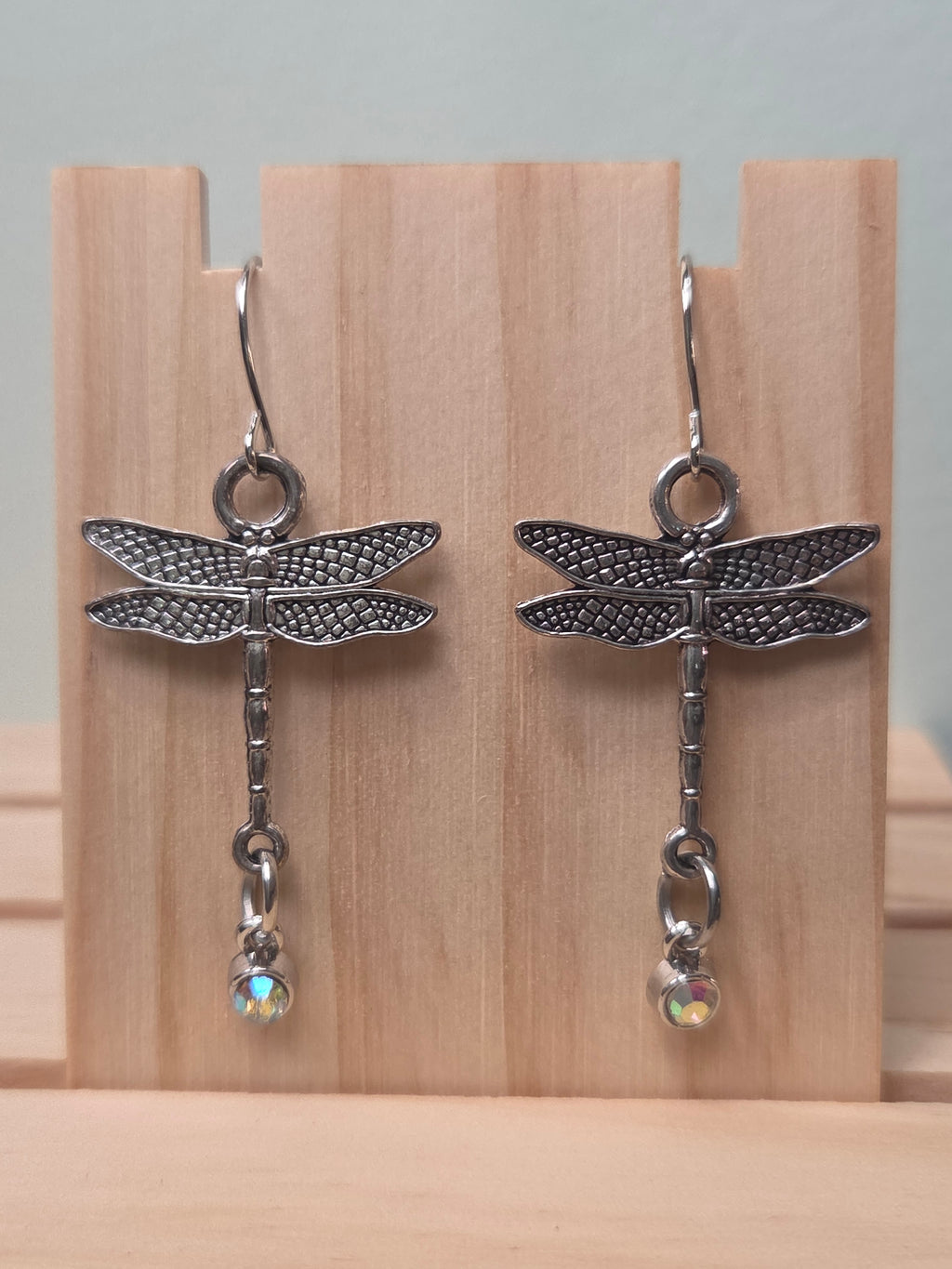 Silver-tone dragonfly dangle earrings with aurora borealis crystal drop, shown on wood display