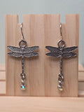 Silver-tone dragonfly dangle earrings with aurora borealis crystal drop, shown on wood display